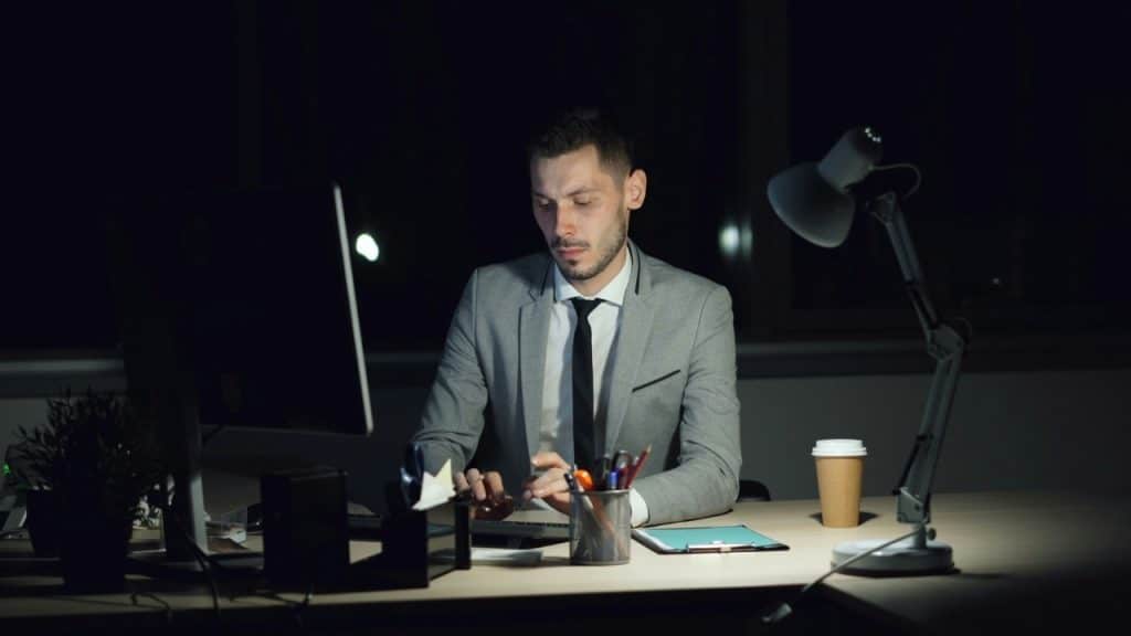 A man in a grey suit works at a computer in a dark office room