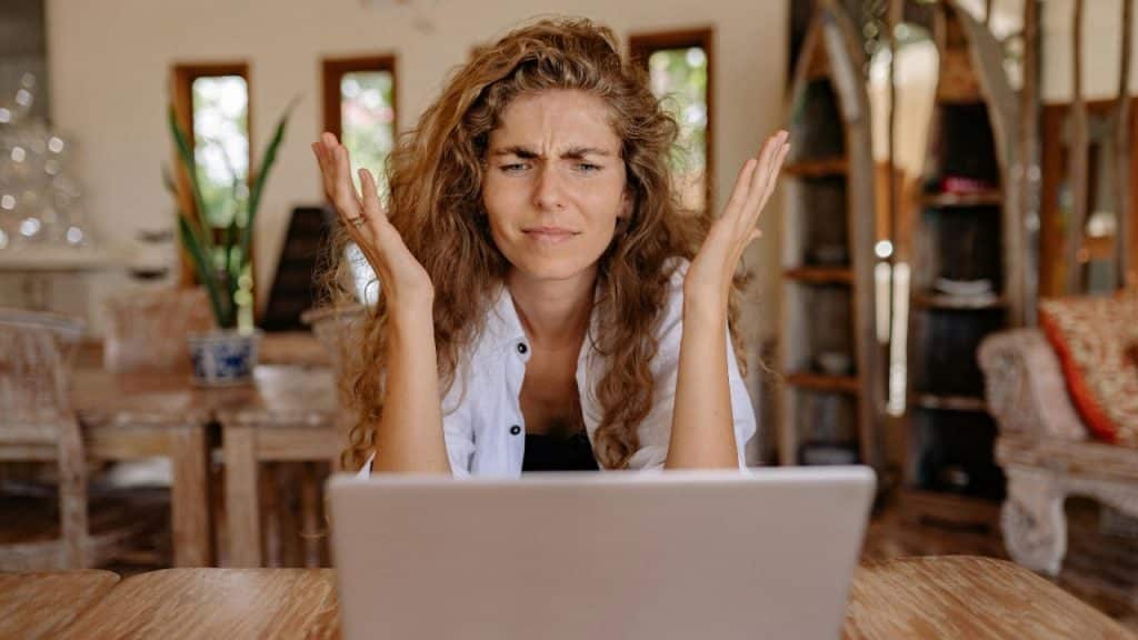 A woman with curly hair sits behind a laptop with her hands raised in the air.