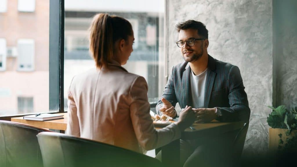 A man and woman in business casual attire sit across from each other at a table.