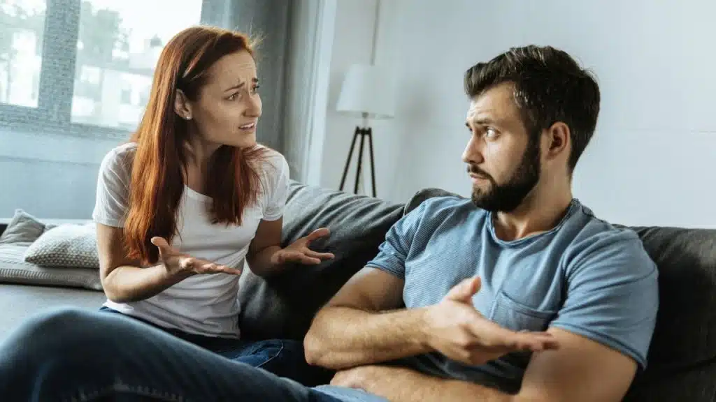 A woman with red hair gestures with open hands while talking to a bearded man.