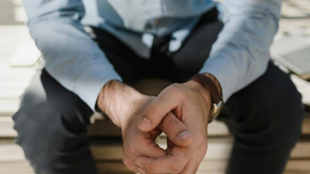 A person sitting with their hands clasped together in front of them.