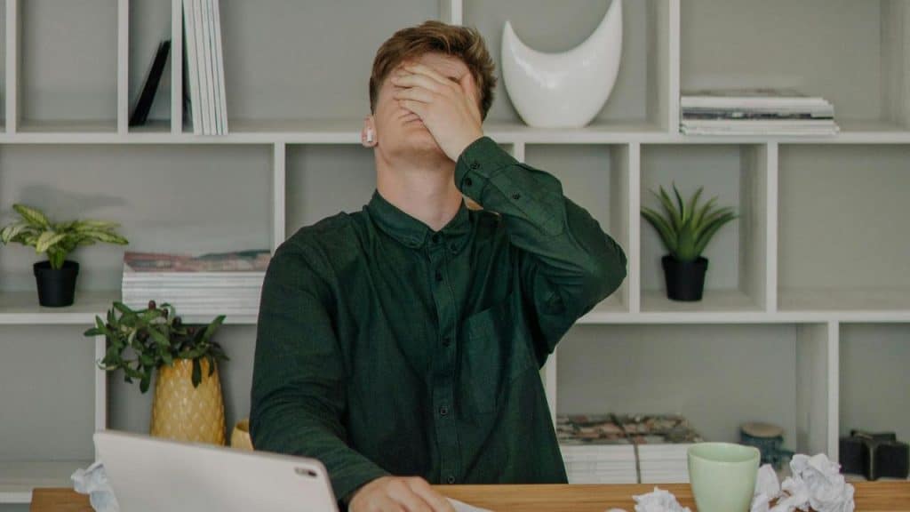 A man sitting at a desk with his hand covering his face in frustration.