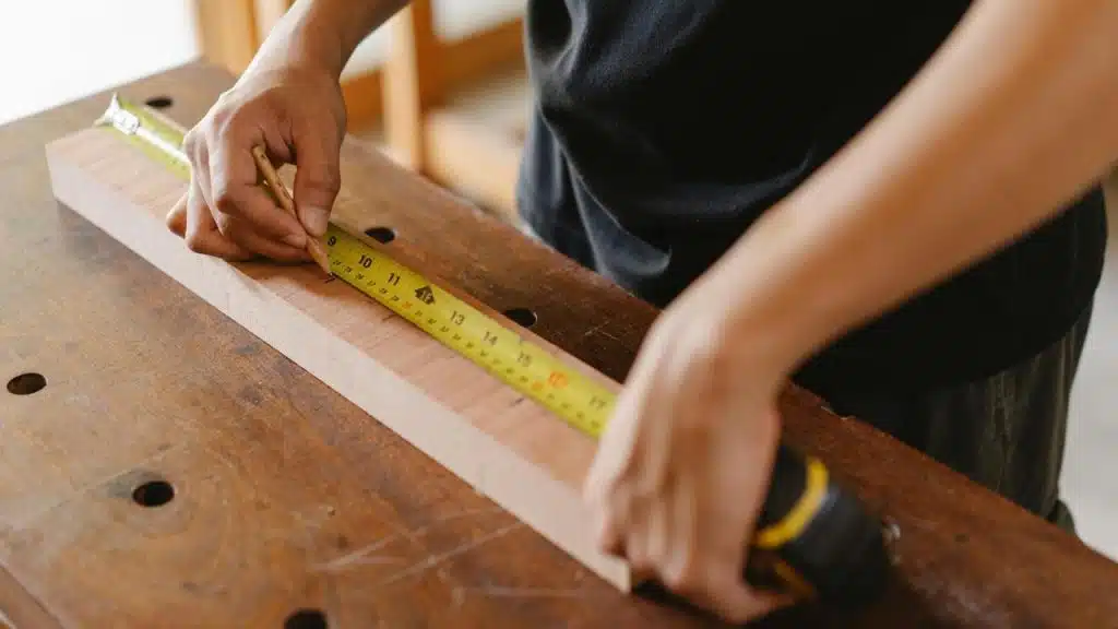 A person measuring a piece of wood with a tape measure on a workbench.