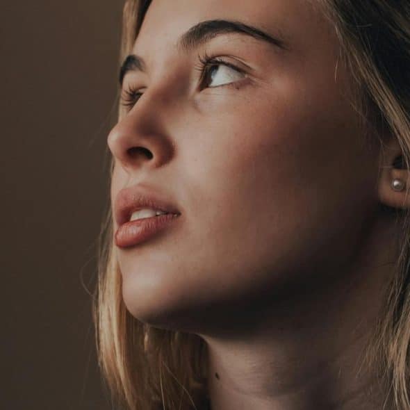 A close-up of a woman looking upward with a thoughtful expression.