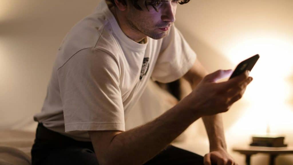 A person sitting on a bed and looking at a smartphone.