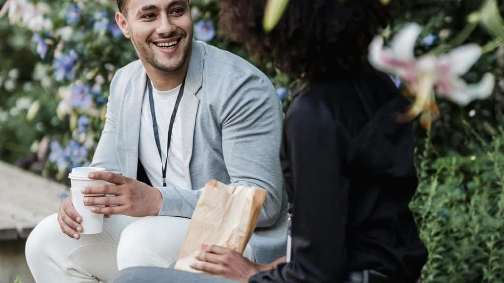 A man smiling and talking with a woman outdoors while holding a coffee cup.