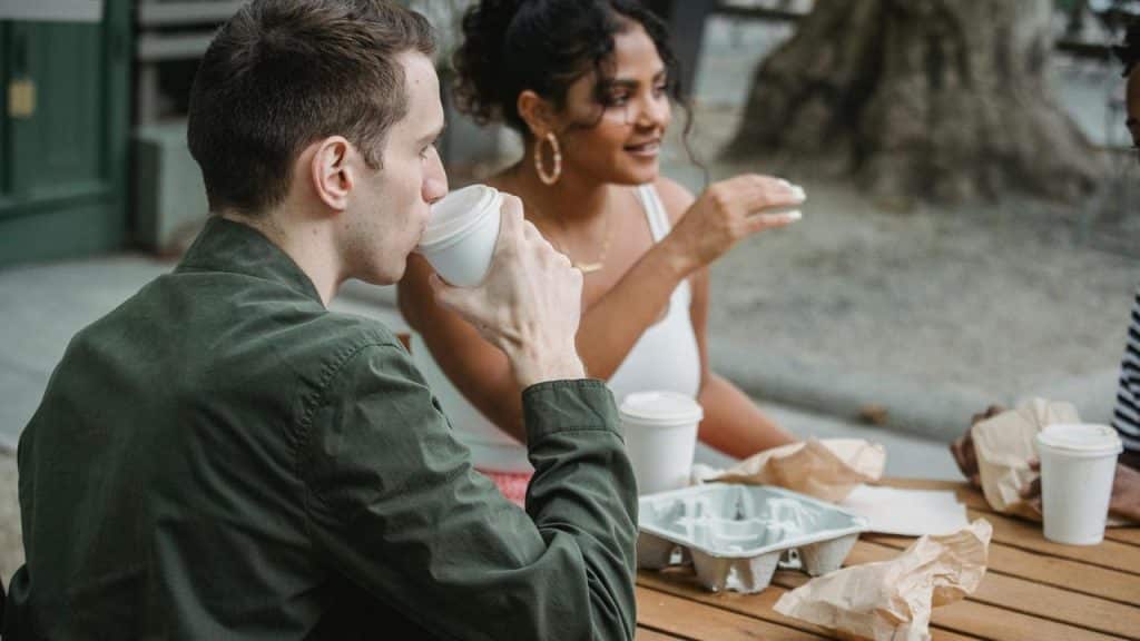 A man and woman sitting at an outdoor table drinking coffee together.