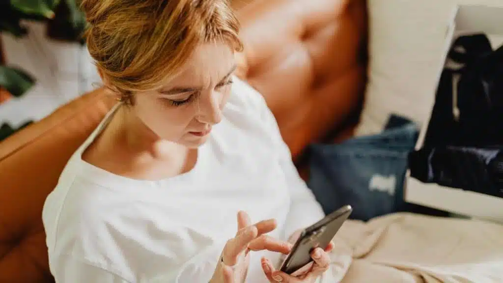 A woman sitting on a couch looking at her smartphone.