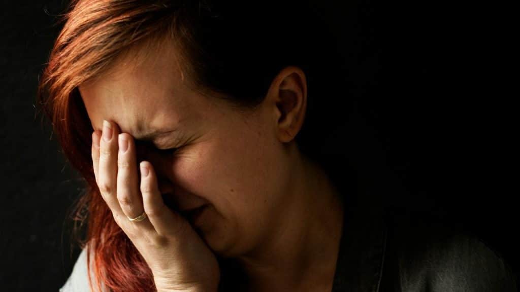A woman covers her face with one hand in low light.