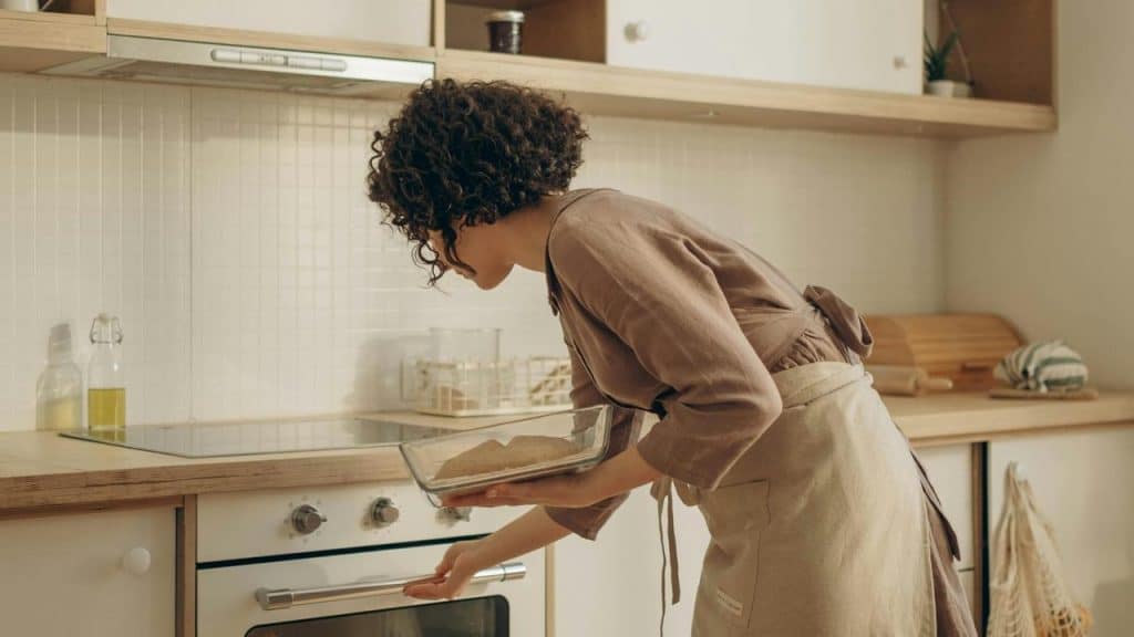 A woman placing a glass baking dish into an oven in a kitchen.