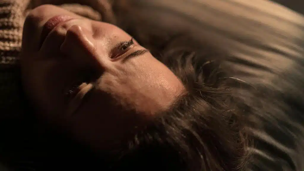 A woman lies on her side in warm light, gazing upward thoughtfully.