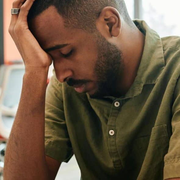 A stressed man resting his head on his hand while sitting at a desk.