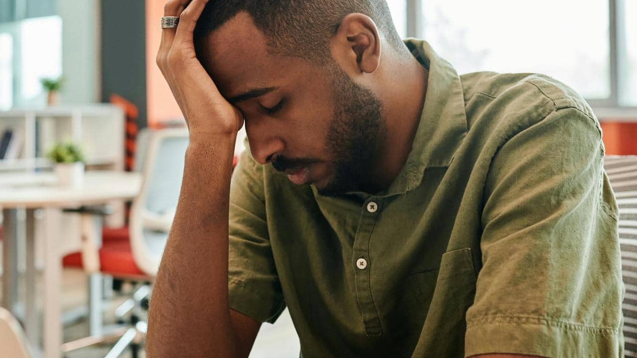 A stressed man resting his head on his hand while sitting at a desk.