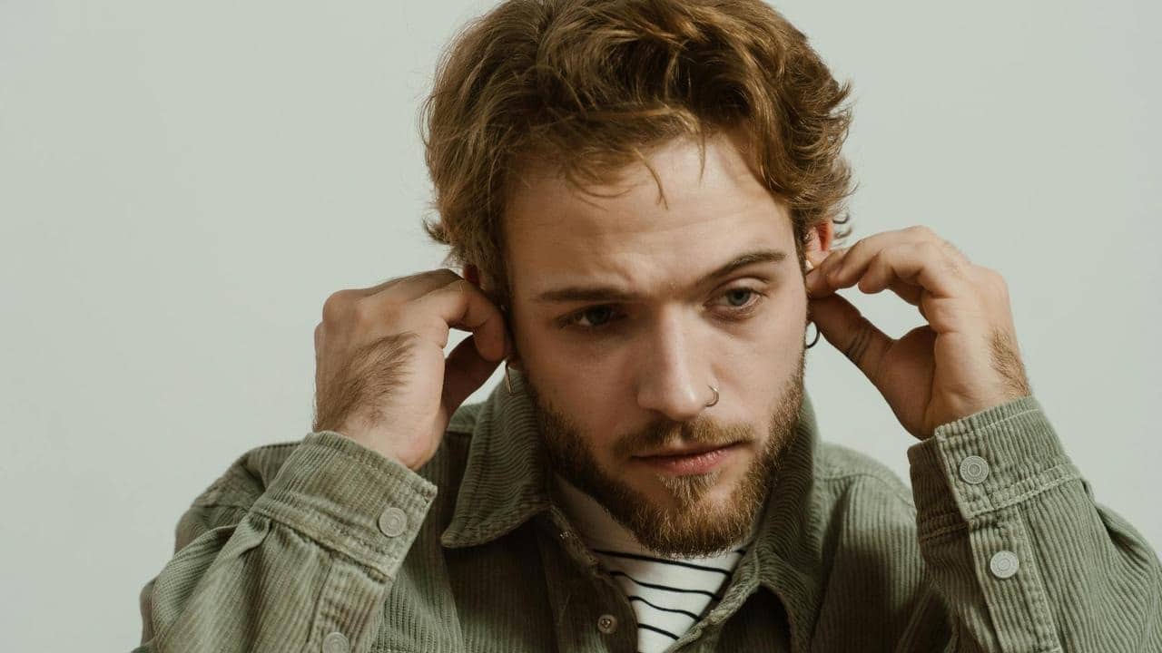 A man adjusting his earphones while looking focused and pensive.