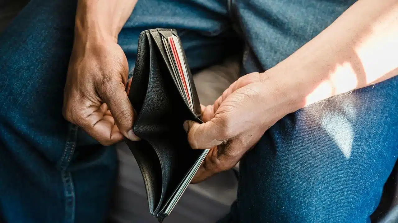 A person sitting with their legs crossed, holding an open empty wallet.