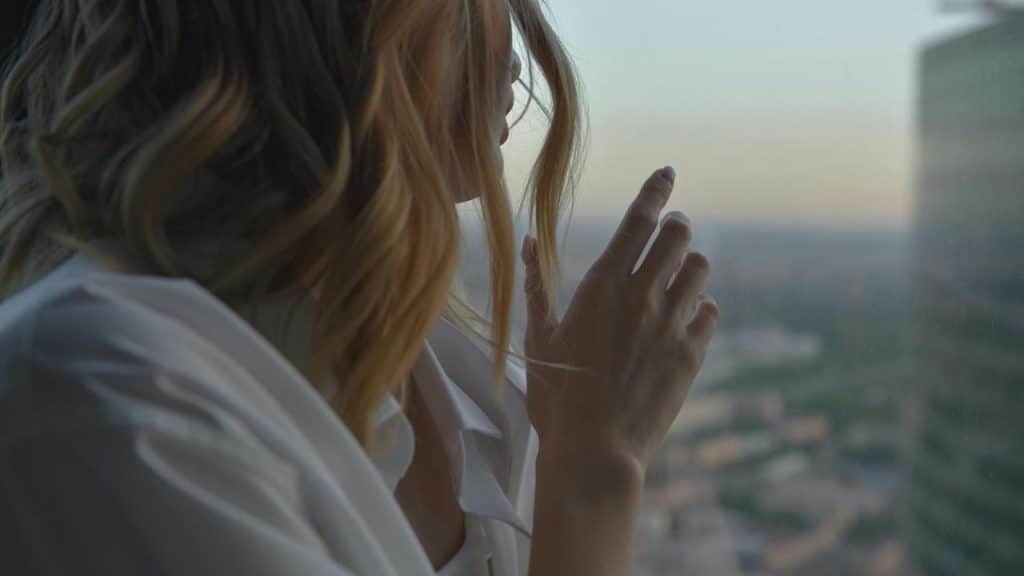 A person standing by a window, gently touching the glass while looking outside.