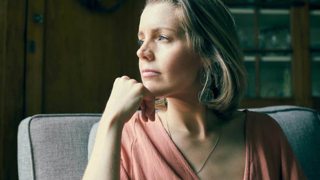A woman gazes thoughtfully out a window while resting her chin on her hand.