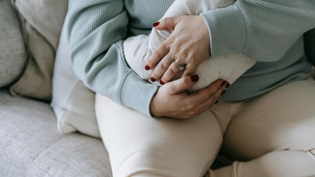 A person sitting on a couch holding a baby wrapped in a blanket.