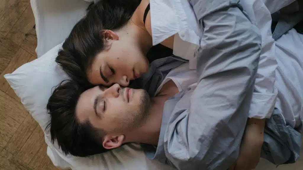A couple lying close together in bed, resting peacefully.
