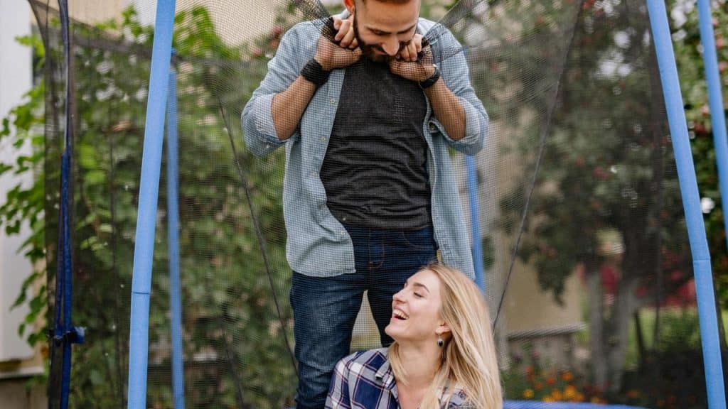 A couple laughing together while playing on a trampoline outdoors.