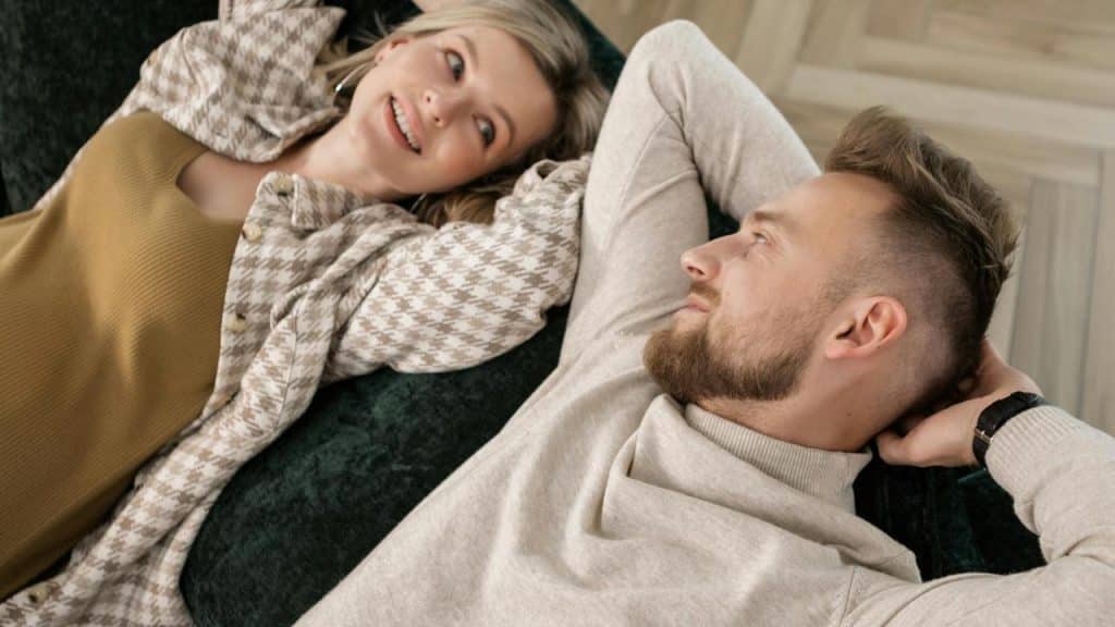 A couple lying on a couch, looking at each other and smiling.