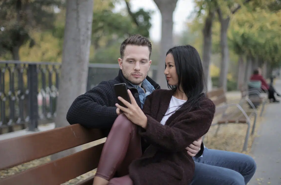 Young couple using smartphone while sitting on bench