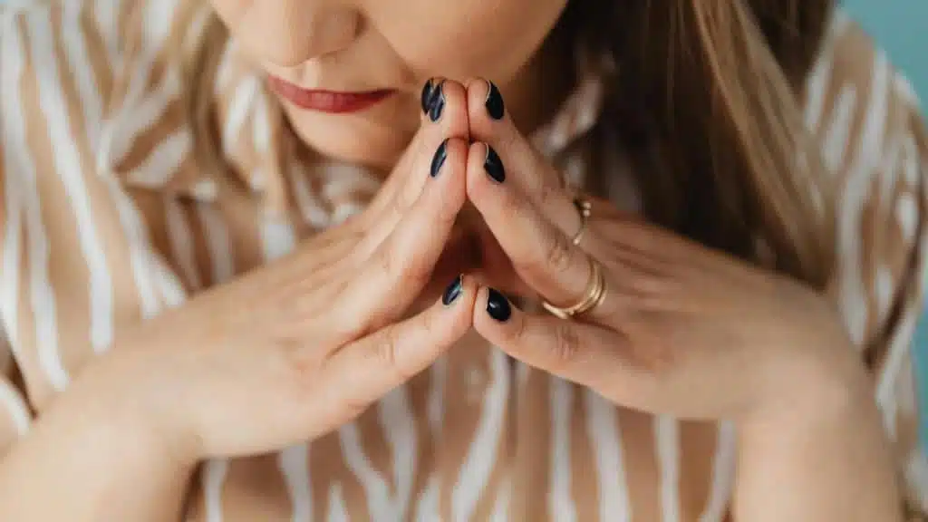 A woman resting her chin on her hands with dark polished nails.