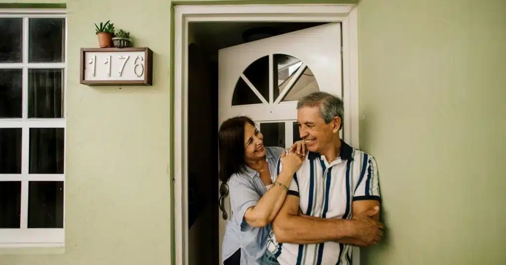 A smiling couple standing together in a doorway outside a home.