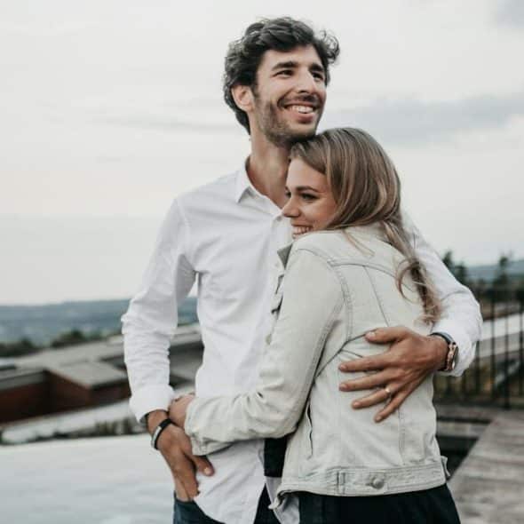 A man hugging his wife in a happy mood while they are standing outdoors.