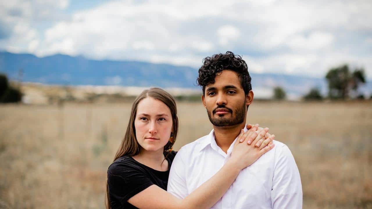 A woman holding a man while they stand in a field.