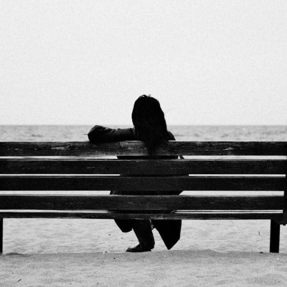 A woman sitting on a bench by the sea side.