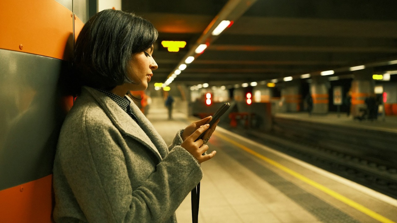 A woman looking at her phone while standing in a subway.