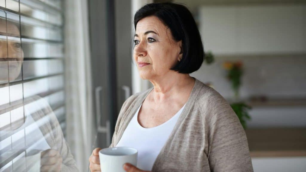A woman holding a mug and looking thoughtfully out a window.