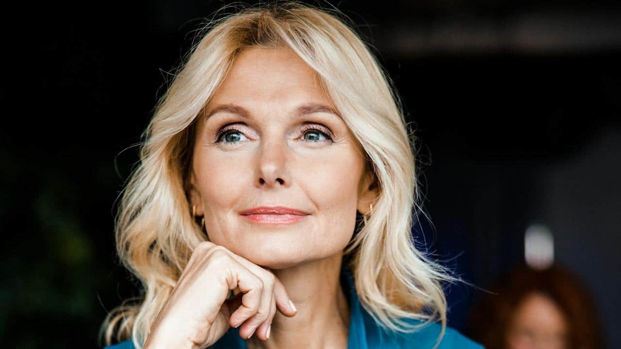 A mature and attractive woman holding her hand to her chin.