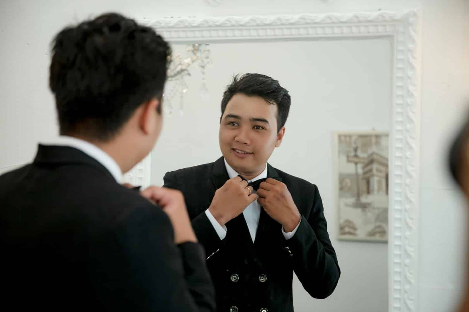 A man fixing his bow tie in front of a mirror