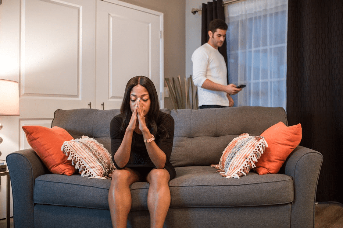 Upset woman sitting on sofa while man stands at the back