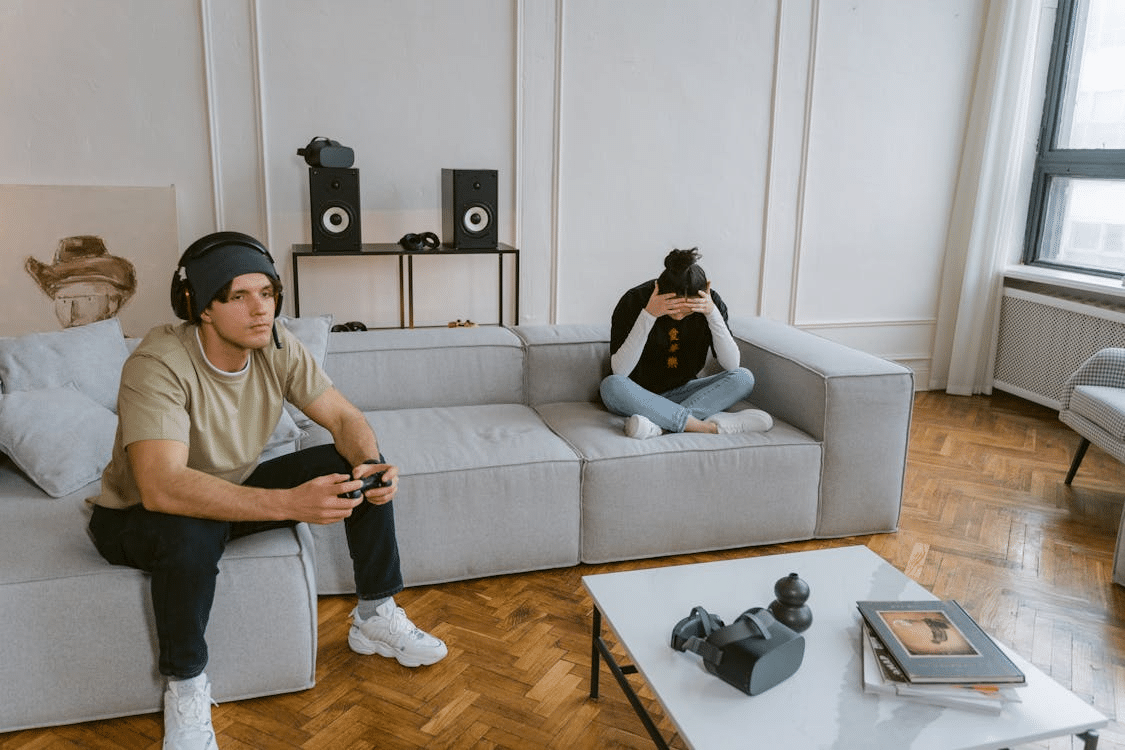 Man playing video games across couch from upset girlfriend