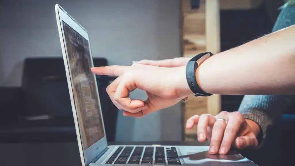 A person pointing at a laptop screen while another person types on the keyboard.