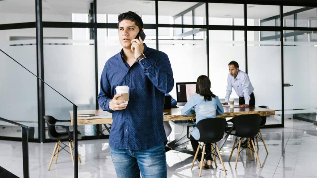 A man talking on a phone while holding a coffee cup in a modern office.