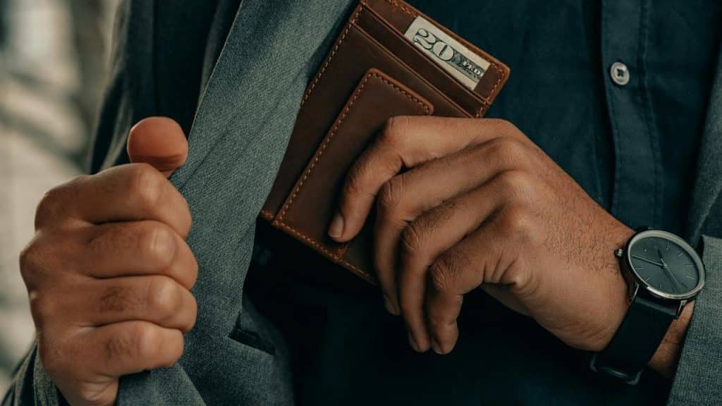 A person placing a leather wallet into the inside pocket of a jacket.