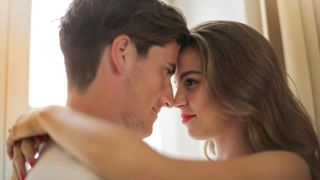 A couple embracing with their foreheads touching and smiling at each other.