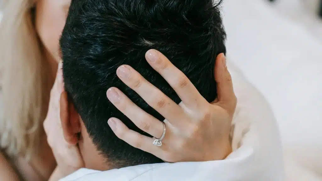 A woman’s hand with an engagement ring gently holding a man’s head.