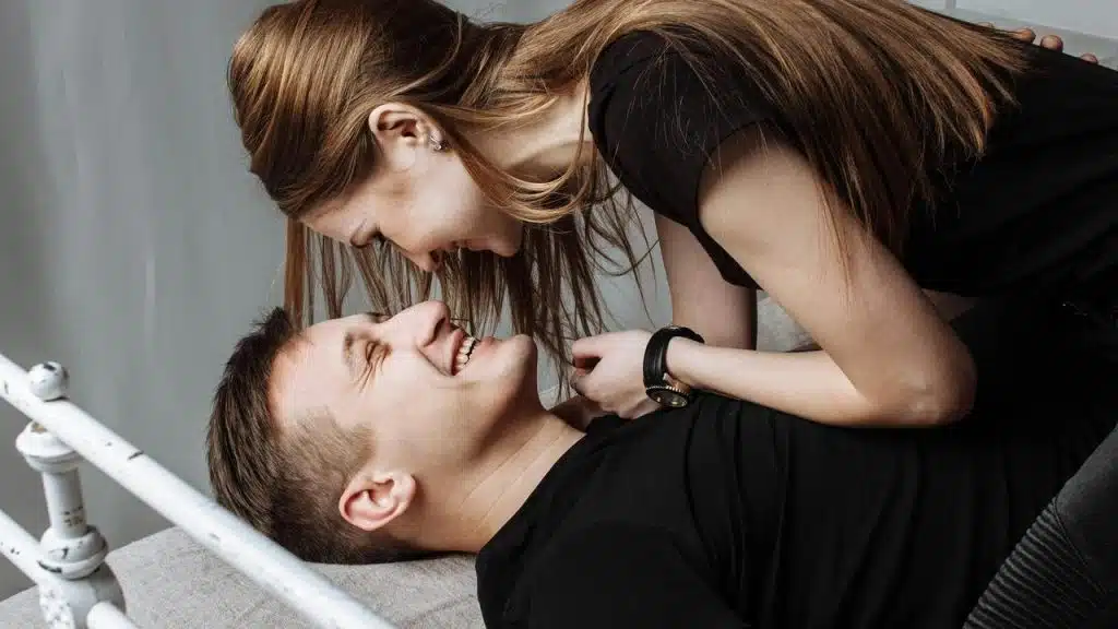 A couple laughing together on a bed.