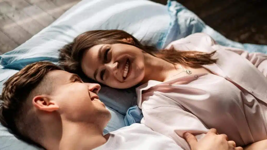 A couple lying in bed smiling at each other.