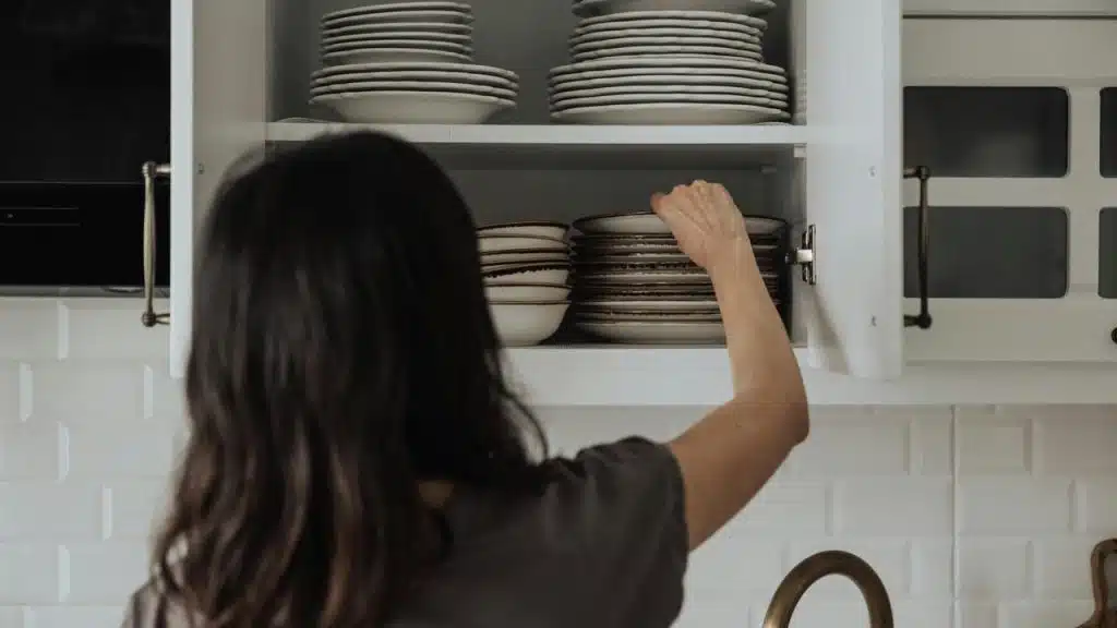 A person reaching into a kitchen cabinet to arrange stacked plates.