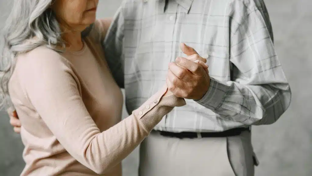 An older couple holding hands while slow dancing together.