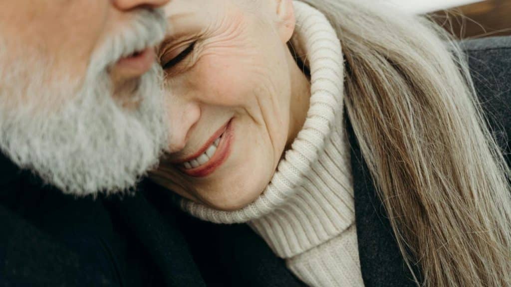 An older couple cuddling closely with the woman smiling against the man's cheek.