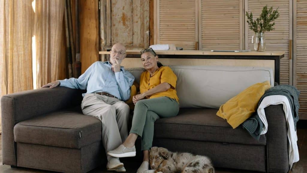 An older couple relaxing on a sofa with a dog resting at their feet.