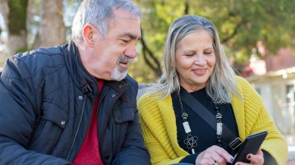 An older couple sitting outdoors and looking at a smartphone together.