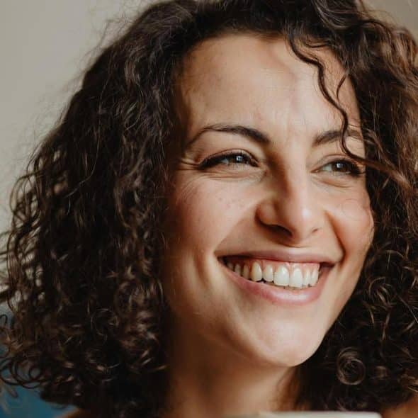 A close-up of a smiling woman with curly hair indoors.
